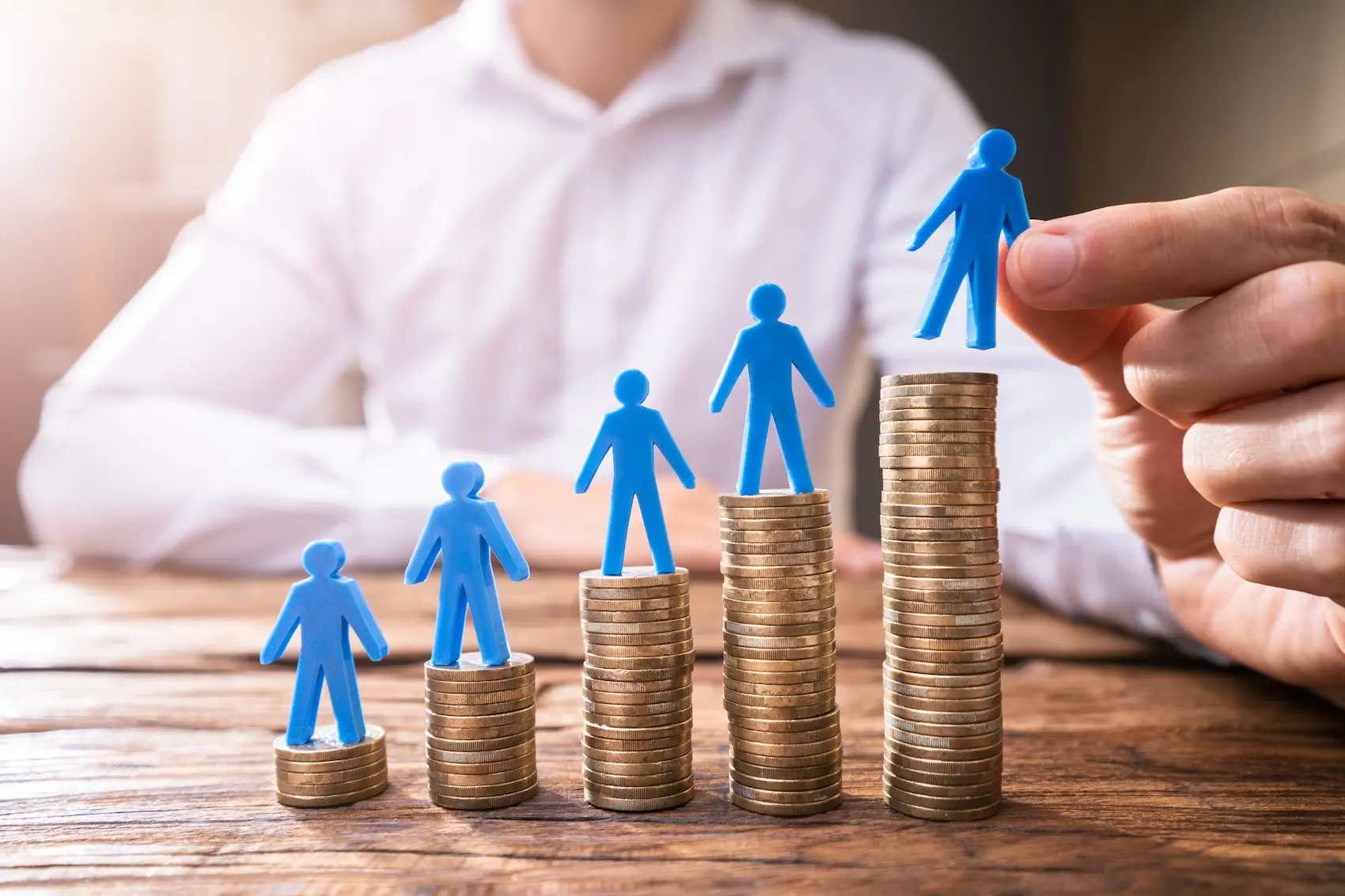 person placing toy people on stacks of coins